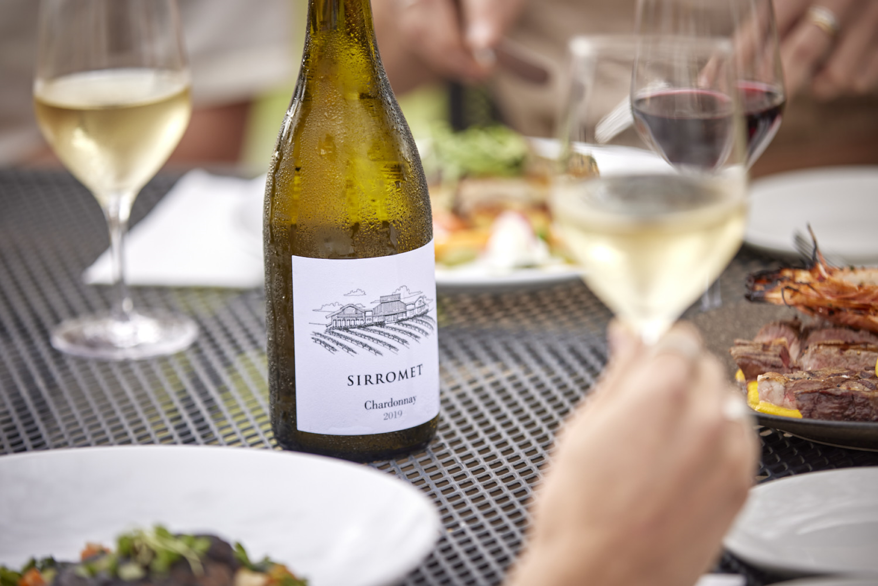 Hand holding wine glass with wine with others on a table